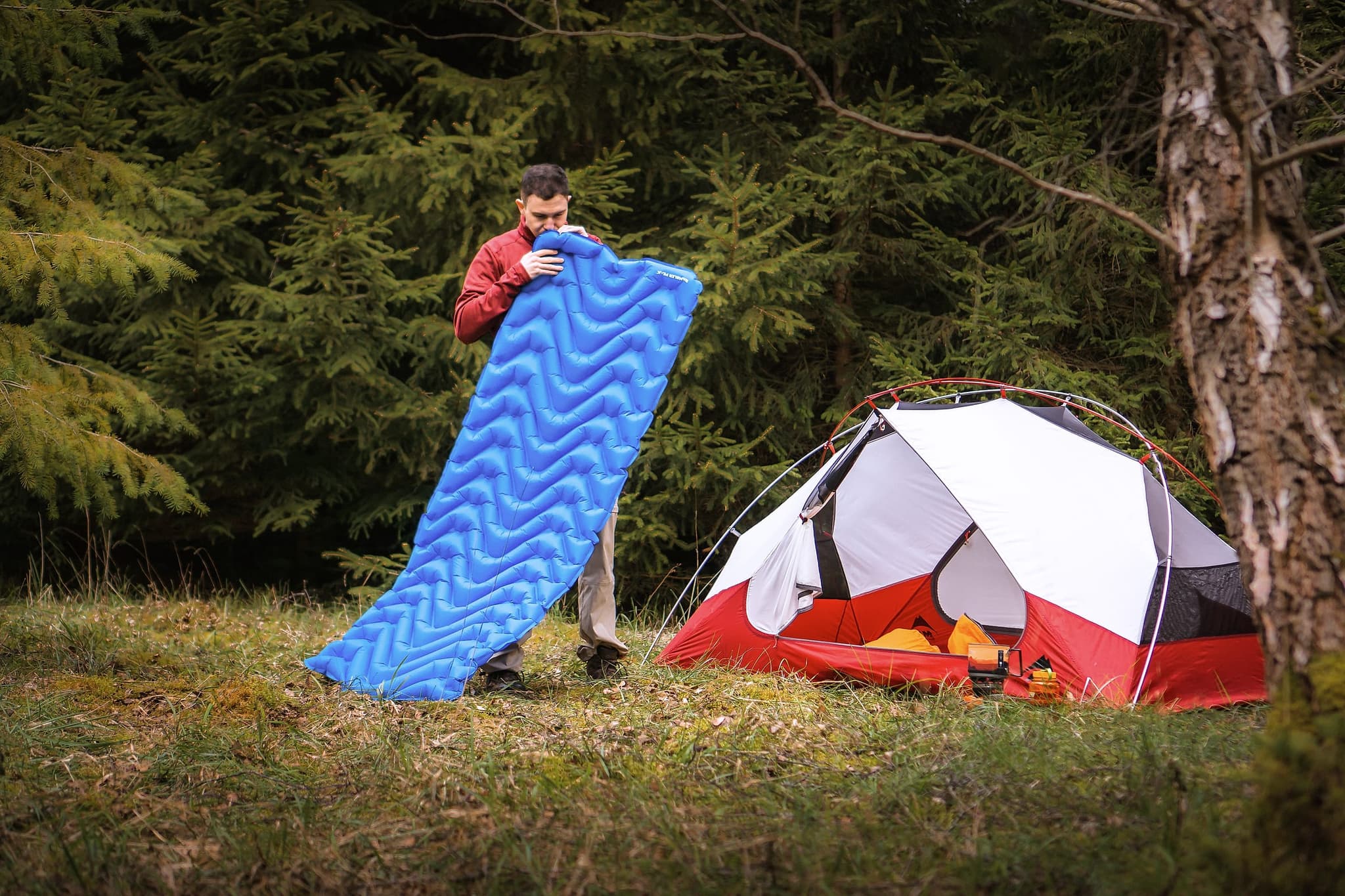 A camper unrolling the DreamLite mat beside a tent in a forest clearing