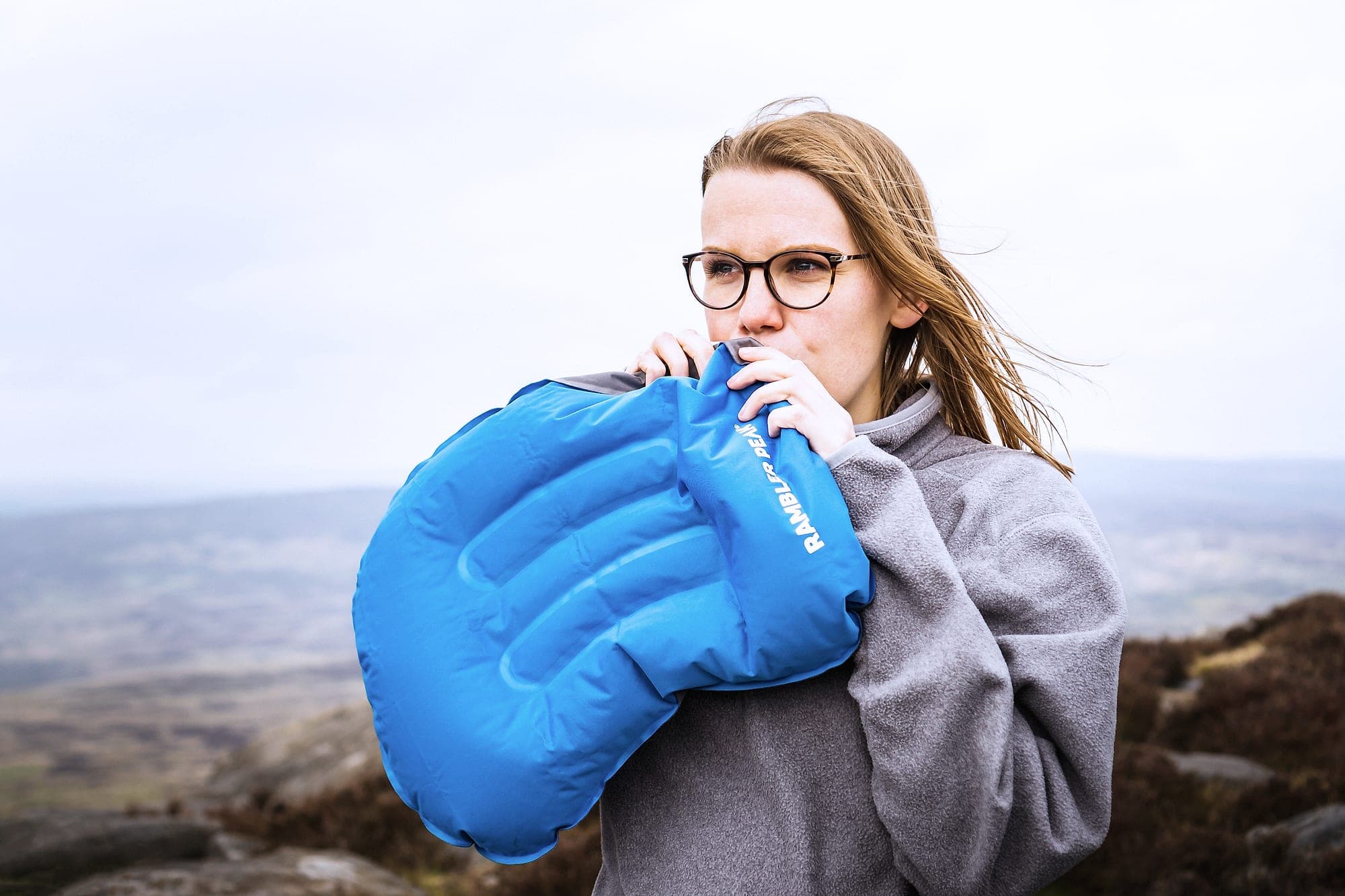 A camper inflating the ergonomic pillow in a single breath on a Peak District edge